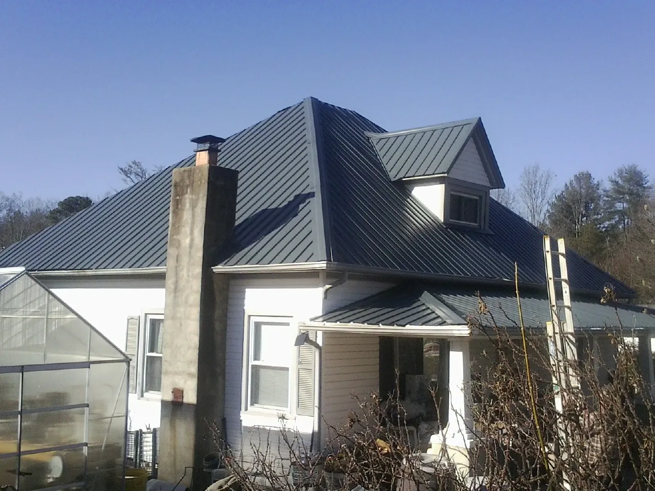 Dark blue standing seam metal roof on a white farmhouse with dormer — Slate & Tile Roof Repair by Roofing Brothers in Halsey
