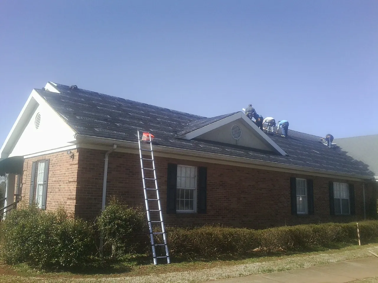 Crew tearing shingles off a brick ranch roof with a ladder set — Metal Roof Repair work by our crew in Halsey