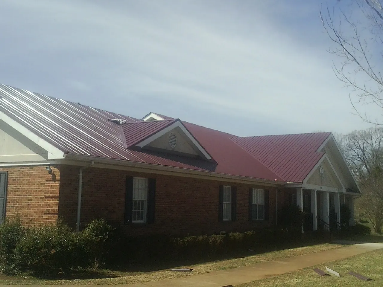 Red metal roof with gabled entries on a long brick building, from a Hail Damage Roof Repair job in Halsey