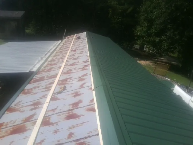 Old rusted panels beside newly installed green metal roofing — Wind Damage Roof Repair by Roofing Brothers in Halsey