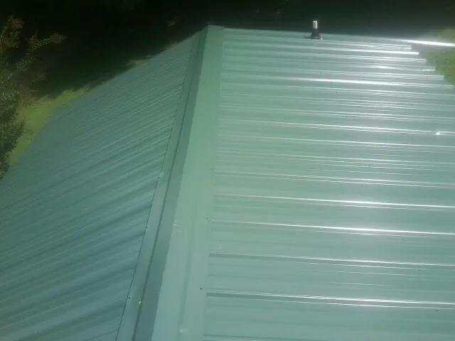 New green metal panels meeting at the ridge of a roof — Flat Roof Repair work by our crew in Halsey