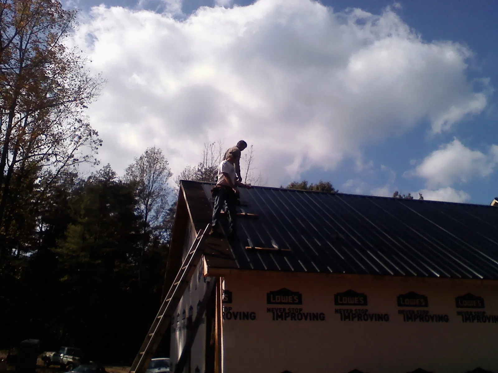 Roofer fastening dark metal panels high against a cloudy sky, from a Roof Inspection job in Halsey