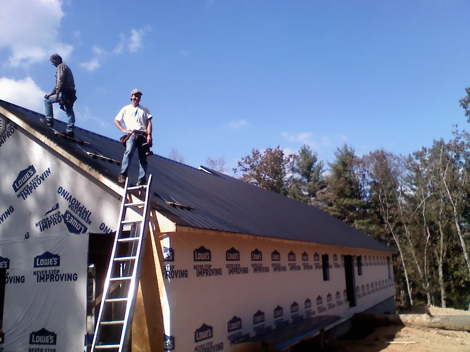 Two roofers standing on a long dark metal roof over a wrapped building in Halsey