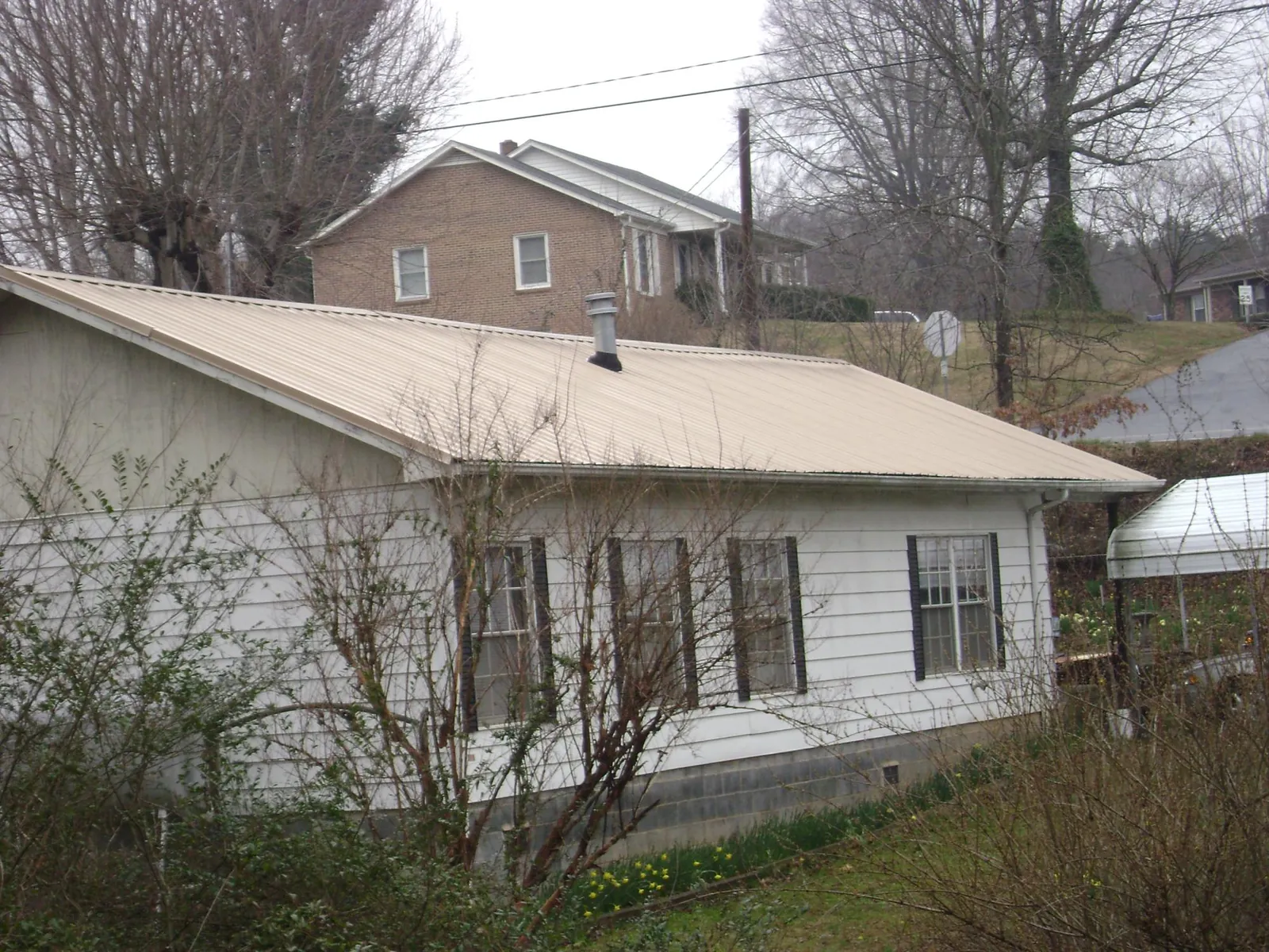 Tan metal roof on a white sided house set into a hillside — Commercial Roofing by Roofing Brothers in Halsey